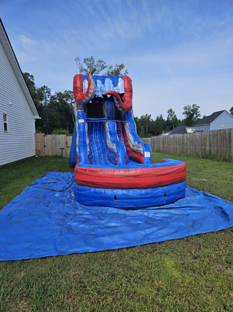 Blue and red water slide with a splash pool set up on a tarp in a backyard