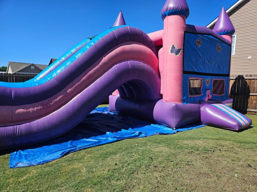 Purple and pink bounce house combo with slide in a backyard